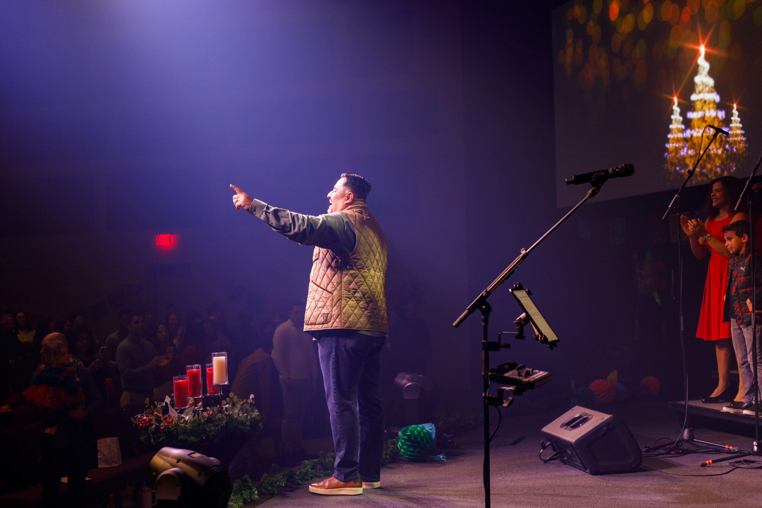 pastor preaching from stage on christmas eve, with lit candles in the foreground